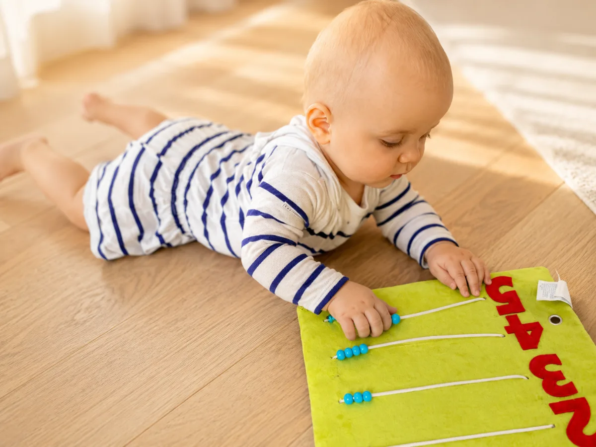 Bébé faisant glisser les perles de l'abaque en tissu Kitibook, geste de motricité fine